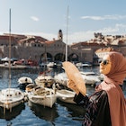 portrait of young European Muslim woman with hijab holding a hand fan and looking at the camera. Sea is in the background. She is happy and relaxed..; Shutterstock ID 1649185399; your: Claire Naylor; gl: 65050; netsuite: Online ed; full: Best time croatia