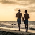 Young homosexual couple walking on the beach of Varadero during sunset, having a drink, talking and having fun together, Cuba.