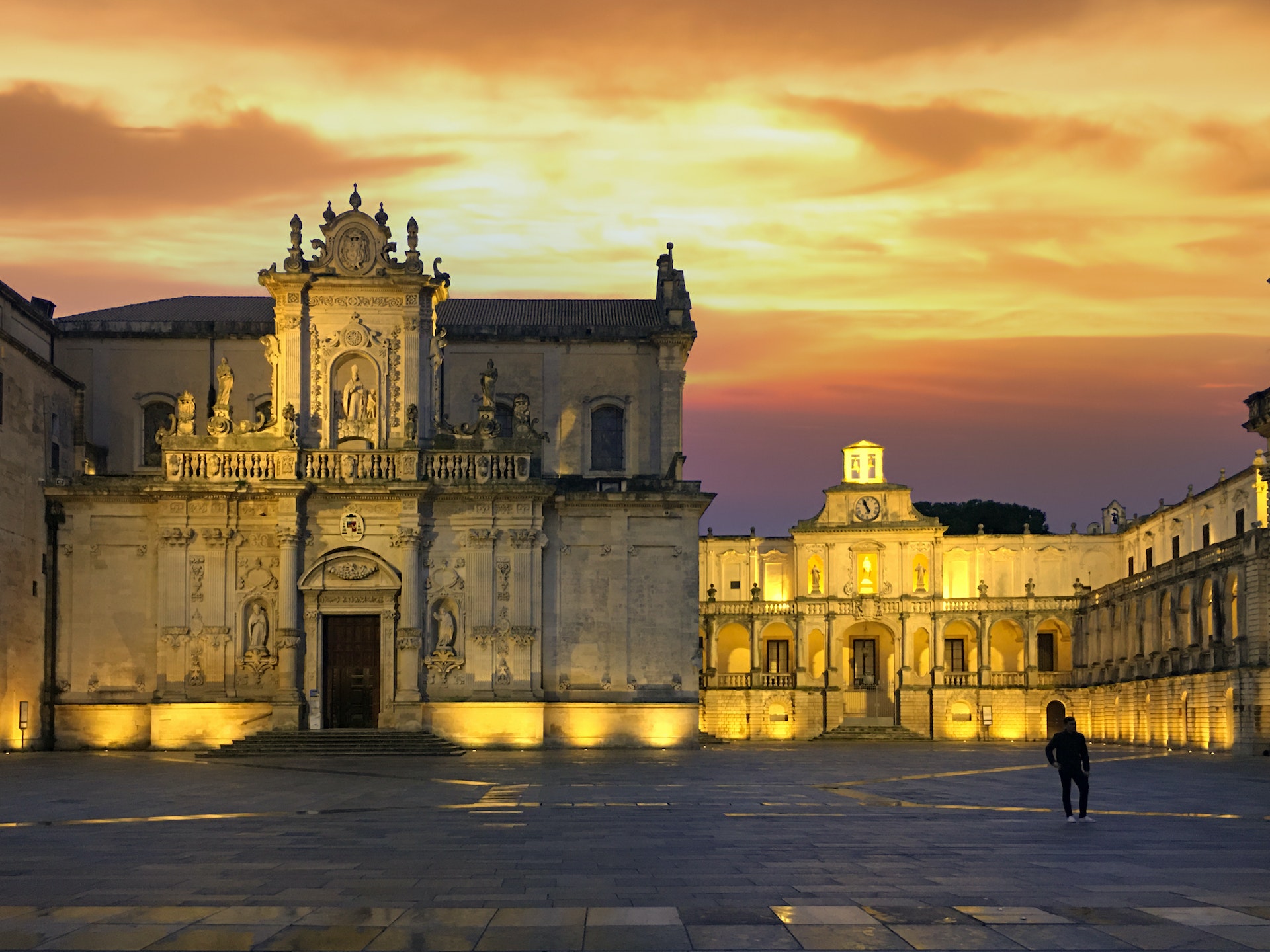 Sunset behind Lecce Cathedral as a person walks through the plaza