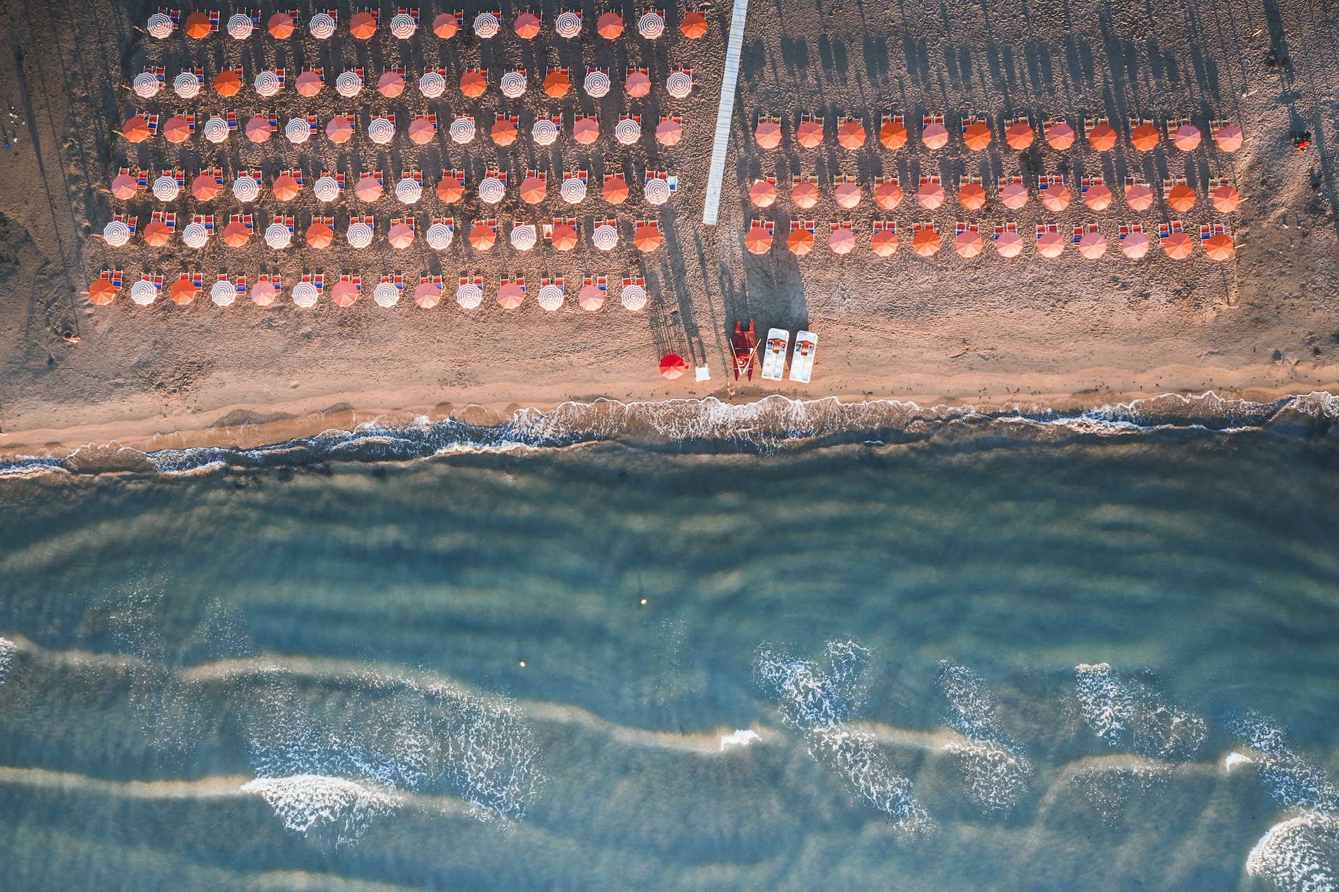 Aerial view of sunshades on sand beach washed by waves