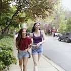 Two young Generation Z women, with long dark hair, laugh while walking along the street, while wearing casual summer clothing.
1369762415
Two women walking arm in arm down a Chicago street