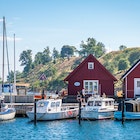 Small boats are docked in front of two red triangular buildings on a sunny day on Ven island, Sweden