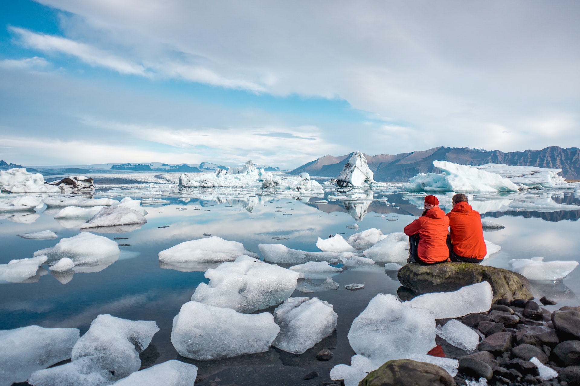 A couple sit on the edge of a lagoon filled with icebergs 
