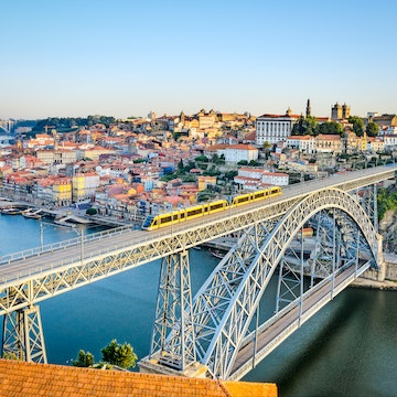 A metro train crosses the Dom Luiz bridge with the historic city of Porto beyond.
