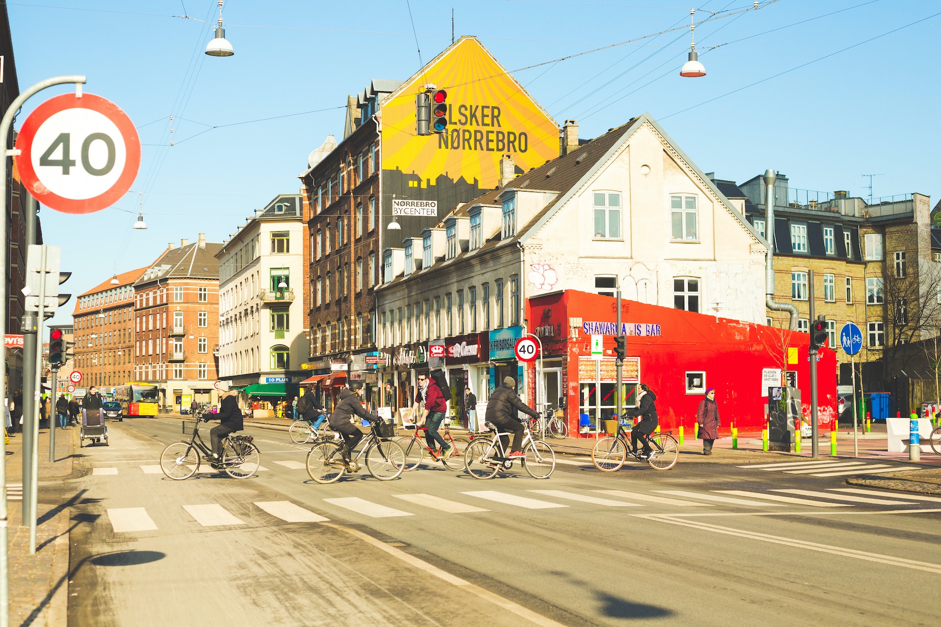 Cyclists ride through the hip streets of a city neighborhood, with independent shops and street art murals