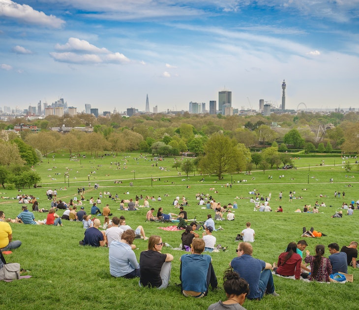 London, UK - April, 2018. Breath-taking panoramic scenic view of London cityscape seen from a crowded Primrose Hill park on a sunny spring afternoon.